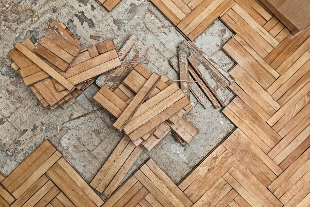 Water Damaged wooden parquet flooring with loose wood pieces on a concrete floor.