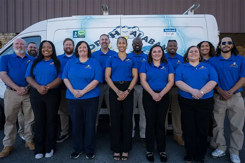 A group of twelve people in blue shirts standing in front of a white van with logos licensed restoration company in North Alabama