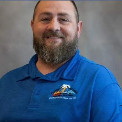 Bearded man smiling, wearing a blue polo shirt with a colorful embroidered logo.