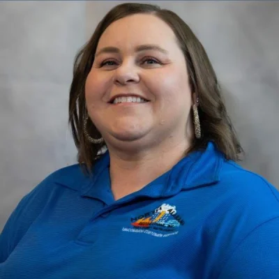Smiling woman with shoulder-length brown hair wearing a blue polo shirt with a logo.